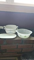 Pyrex casserole dish, Corning Ware casserole dish, and white ceramic serving tray on brick hearth.