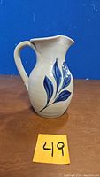Front view of the off-white ceramic pitcher showing the blue leaf decoration.