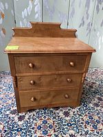 Front view of solid wood dresser showing three drawers with wooden knob pulls and decorative top backboard