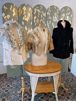 Full view of the 3 fur pieces displayed on mannequins including white faux fur vest, beige mink bolero jacket, and black double-breasted broadtail jacket with mink collar.
