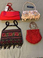 Five evening purses laid out on a green surface showing their overall shape, material, and style variety