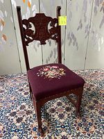 Full view of Gothic Victorian chair showing needlepoint floral seat and carved face backrest.