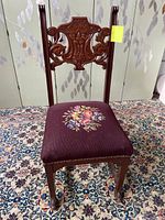 Front view of the chair showing floral needlepoint upholstery on seat and carved wooden legs ending in claw feet.