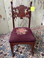 Full view of Gothic Victorian dark wood chair with burgundy floral needlepoint seat and ornate carved face backrest.