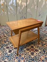 Front and side view of Mid-Century Modern oak veneer end table showing top surface, drawer front, lower shelf and tapered legs with brass tips.