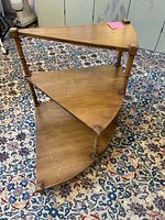 Mid-Century Modern spiral design end table with three triangular wood grain shelves, tapering legs, placed on a patterned carpet.