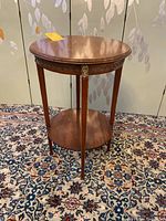 Full side view of the round two shelf occasional table showing wood finish and brass embellishments on legs and top edge.