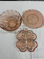 Three pink depression glass pieces: salad bowl, cake plate with handles, and 4-leaf clover shaped serving dish.