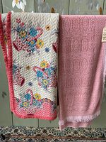 Both the vintage quilt and bedspread hanging over a rack showing the quilt's floral pattern and the pink bedspread with visible fringe detail.