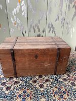 Front view of rectangular wooden shipping chest showing wrought iron bands and central keyhole.
