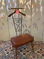 Full view of the valet bench showing brown vinyl cushioned seat, turned wooden legs, and wrought iron back with wooden hanger bar.