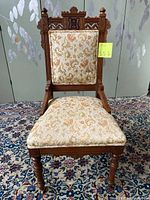 Front view showing the carved wood top rail, upholstered backrest and seat, and turned legs with wheels at the front.