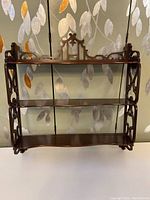 Front view of the three-tier chinoiserie style wooden wall shelf showing shelves and ornamental top design.