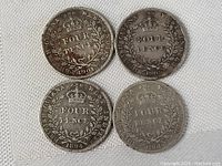 Four British Guiana and West Indies four pence silver coins arranged on white fabric, showing reverse sides with crown and denomination.