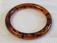 Full view of circular amber bracelet showing polished surface and dark inclusions.