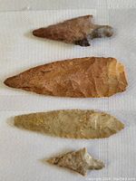Four assorted early arrow and spear heads arranged vertically on a white textured cloth background.