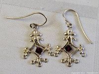 Pair of sterling silver dangle earrings with ornate design and central amethyst stones, displayed on fabric background.