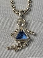 Close-up of one sapphire little girl charm pendant on beaded silver chain.