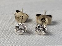 Close-up front view of sterling silver diamond stud earrings on white textured fabric background.