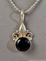 Close-up detail of the pendant showing black onyx stone and intricate silver fleur design.