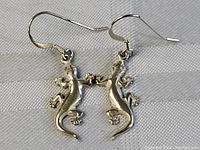 Close-up image showing the front of the sterling silver gecko earrings lying flat on a fabric background.
