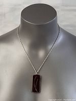 Front view of necklace on mannequin, showing rectangular pendant with dark surface and silver line design on twisted silver chain.