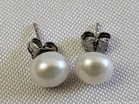 Close-up front view of the pair of sterling silver pearl stud earrings showing the round white pearls and silver posts with butterfly backs.