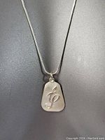 Close-up of pendant showing the engraved symbolic design on a matte silver surface.