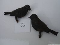 Two hollow tin bird figurines placed side by side with a paper marked '52'