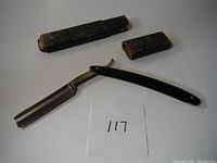 Straight razor with blade extended and leather case pieces laid out.