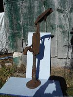 Full view of the antique cast iron water well pump standing upright outdoors against a wooden background.