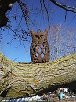 Cast iron owl perched on a tree branch outdoors, showing full front view and scale against natural background.