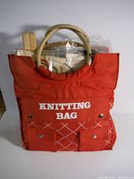 Front view of red knitting bag showing bag color, label, handles, and contents inside.