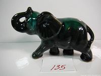 Front left angle view of the ceramic elephant figurine showing the trunk raised and dark green accents.