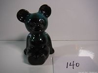 Front view of the ceramic teddy bear figurine showing black and green glaze and seated posture.