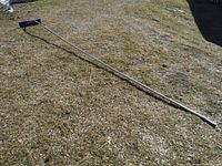 Full length view of the lightweight aluminum handle of the 16-foot roof snow rake scraper lying on grass.