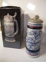 Photo showing the vintage Avon ceramic stein with detailed airplane reliefs and metal hinge lid in front of the original box showing product image