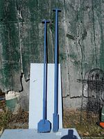 Two blue ice chisels leaning against a white board with an aged wooden background.