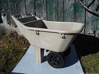 Side angled view of beige plastic garden cart with two black wheels and sturdy handle.