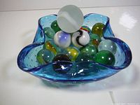 Collection of large marbles with various colors and designs displayed in a blue vintage-style glass dish.