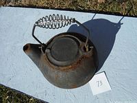 Top view showing rusted cast iron kettle with metal spring handle, spout, and flat base.