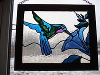 View of the hummingbird design with a textured glass background and wooden frame, showing bird in blue, green, purple next to blue flower.