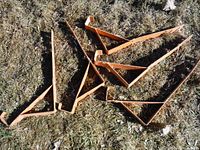 Five orange metal roof jacks laid on grass, showing triangulated frame and hooked teeth for shingle attachment