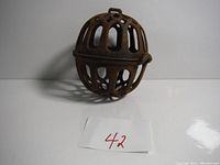 Front angled view of a spherical, cast iron cage ball showing the loop on top and rusted surface.