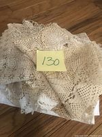 Photo showing a pile of small handmade crochet dollies in beige and cream tones with a note labeled '130'.