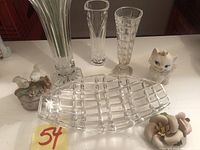 Photo of three clear glass bud vases, one clear glass rectangular tray, and two ceramic decorative figurines arranged on a surface.
