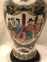 Close-up photo showing detailed hand-painted scene of seated Asian figures and birds on the porcelain vase.