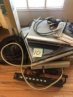 Wide shot of stacked electronics including a DVD player on top of a Technics SL-8200 turntable, power strips, cables, and remote controls on floor near window.