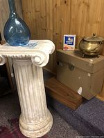 White decorative column and blue glass bottle atop it, with metal container, storage boxes and box of plasters beside it.
