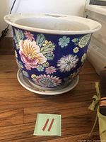 Large blue ceramic pot with colorful floral pattern and attached saucer, placed on wooden floor